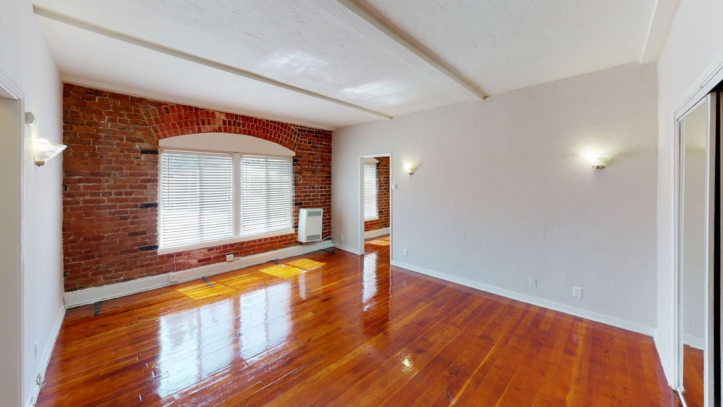 Room with exposed brick wall, hardwood floor, window, and white ceiling.