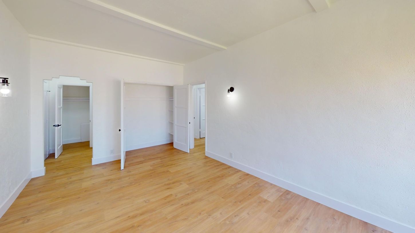 Empty room with wood floors and white walls, two closets, and a hallway.