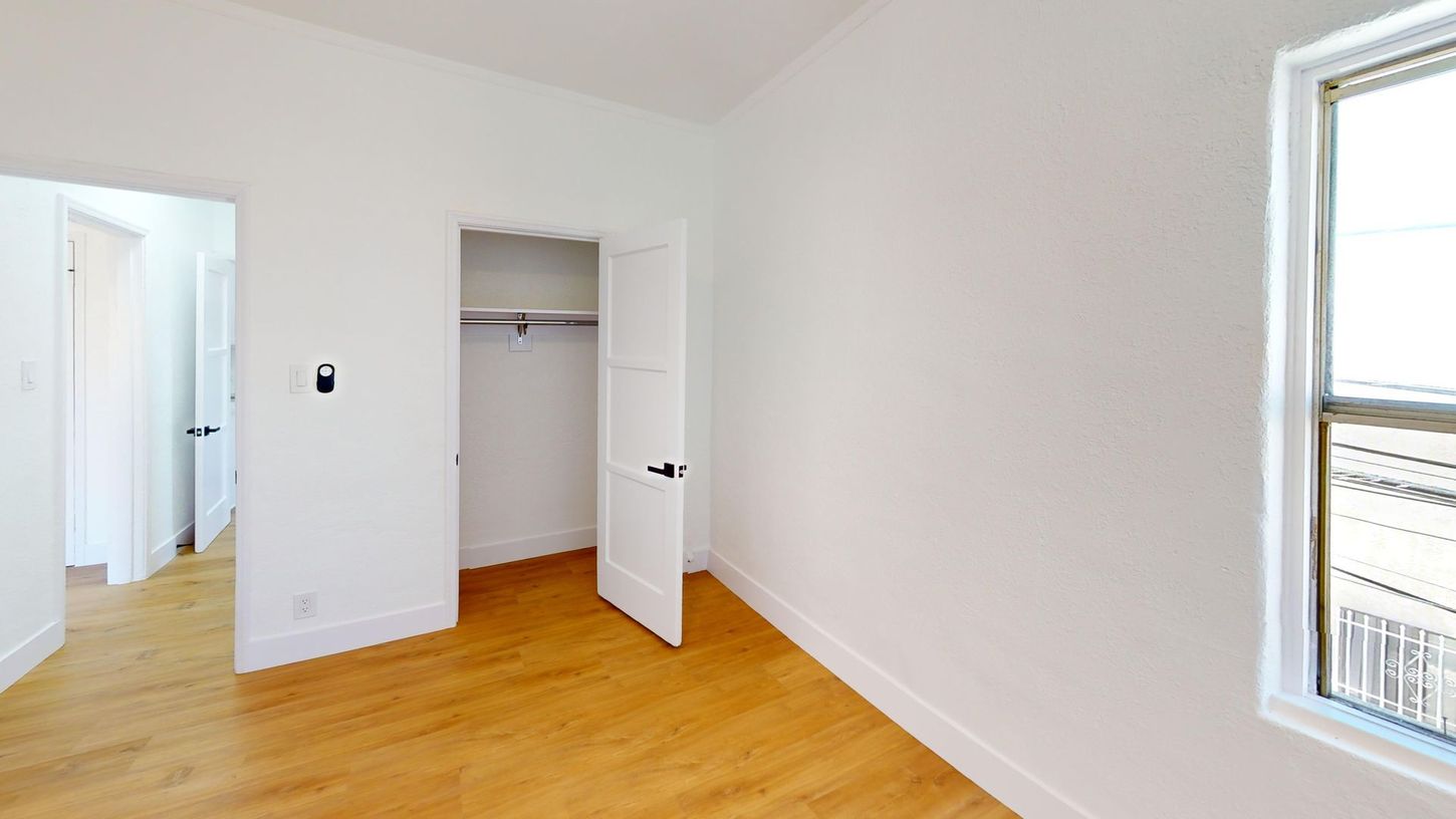Empty room with a closet and a window. Light wood floors, white walls.