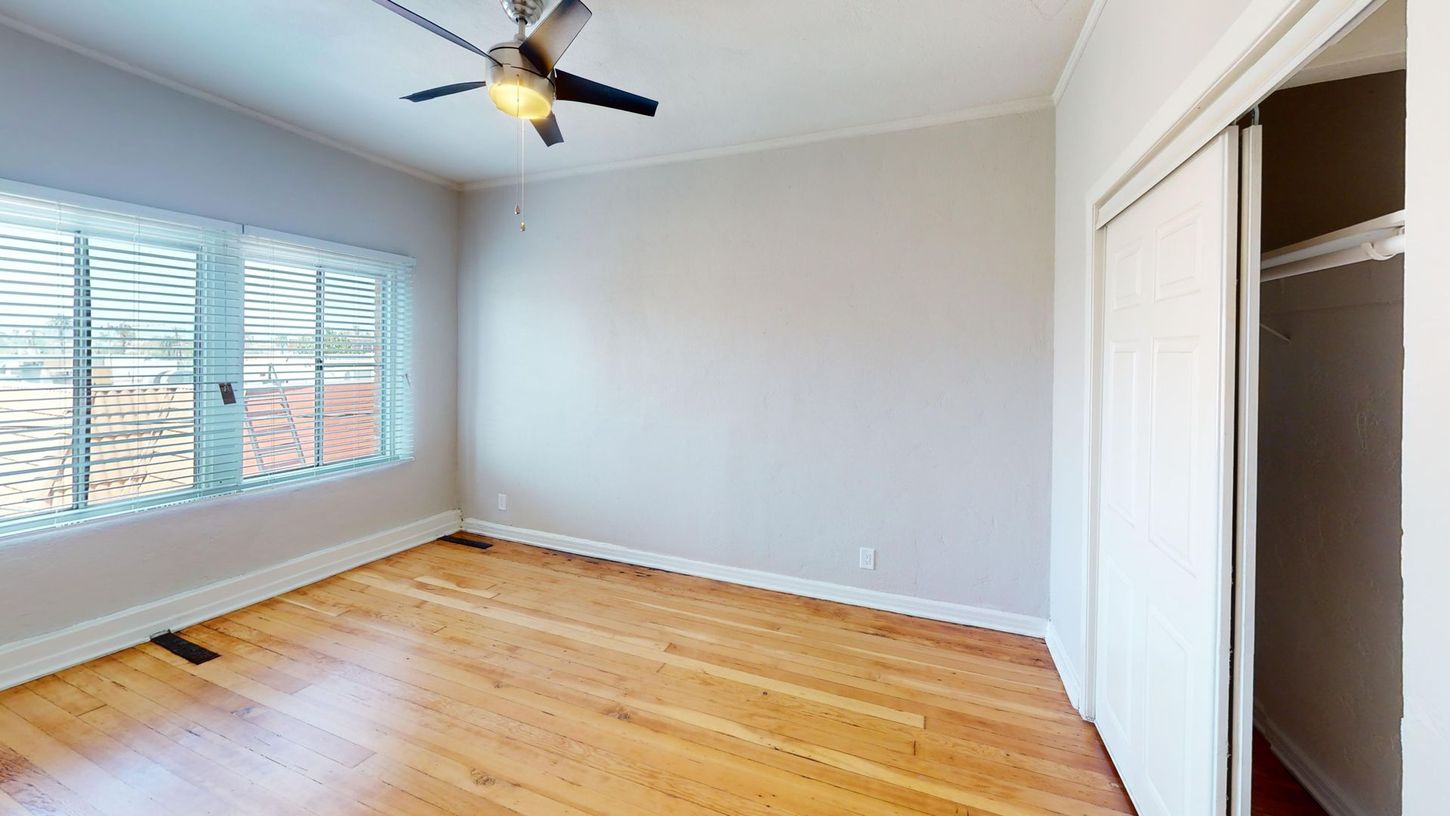 Empty bedroom with hardwood floors, a large window, and sliding closet doors.