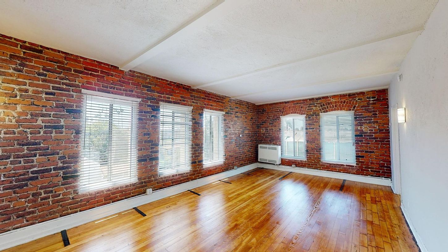 Empty room with exposed brick walls, windows, and wood flooring.