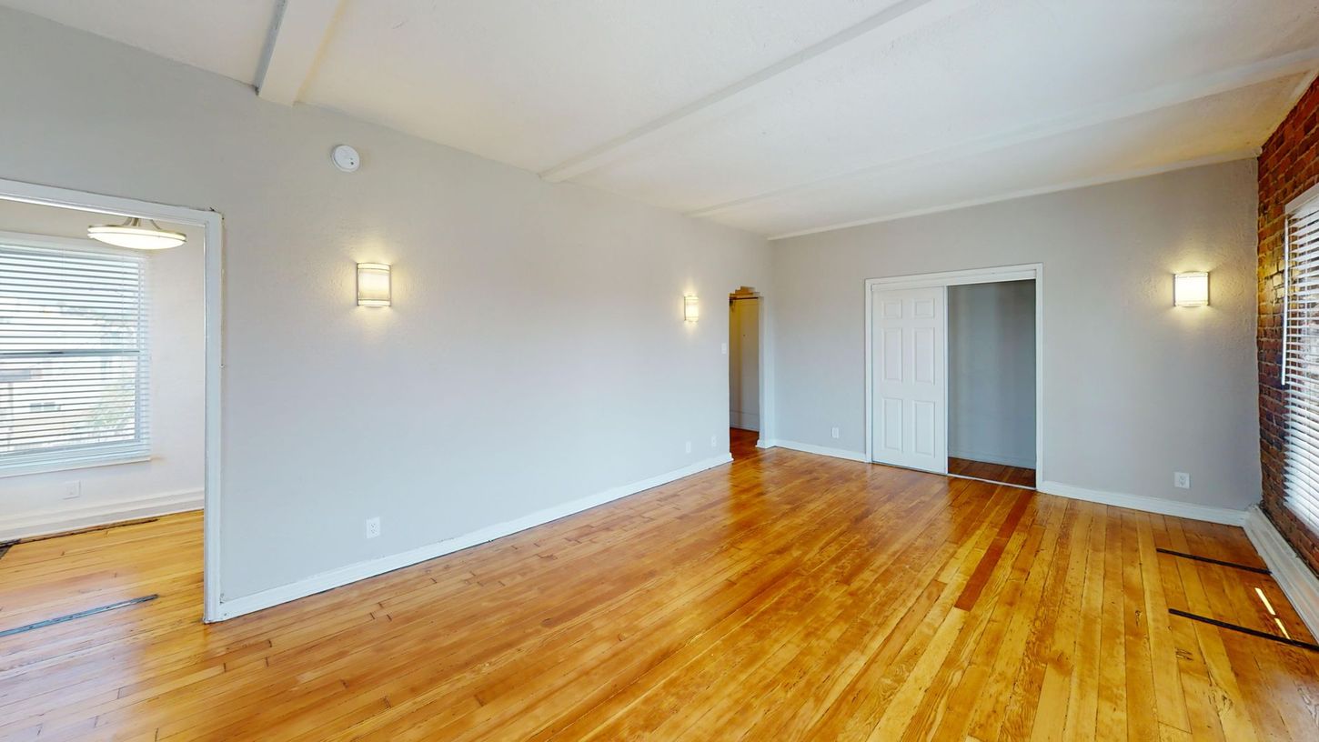 Empty living room with wood floors, pale gray walls, and two wall sconces.
