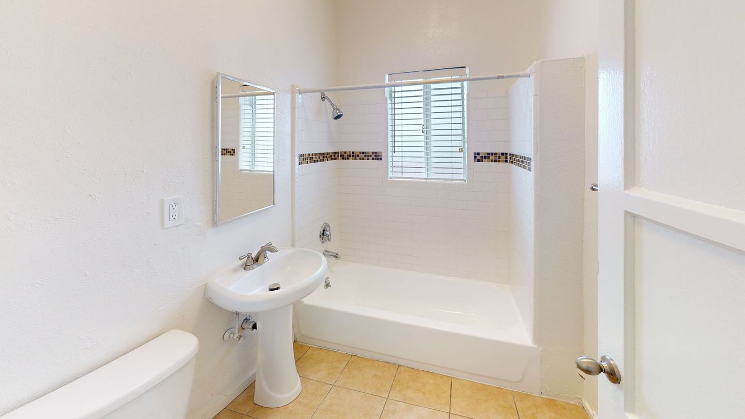 Bathroom with white walls, pedestal sink, tub with shower, and window.