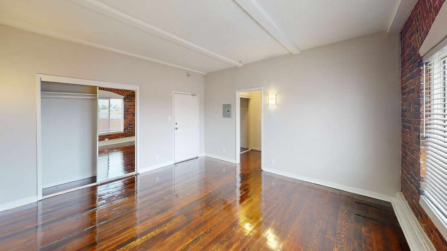 Empty room with hardwood floors, exposed brick, and a sliding door closet.