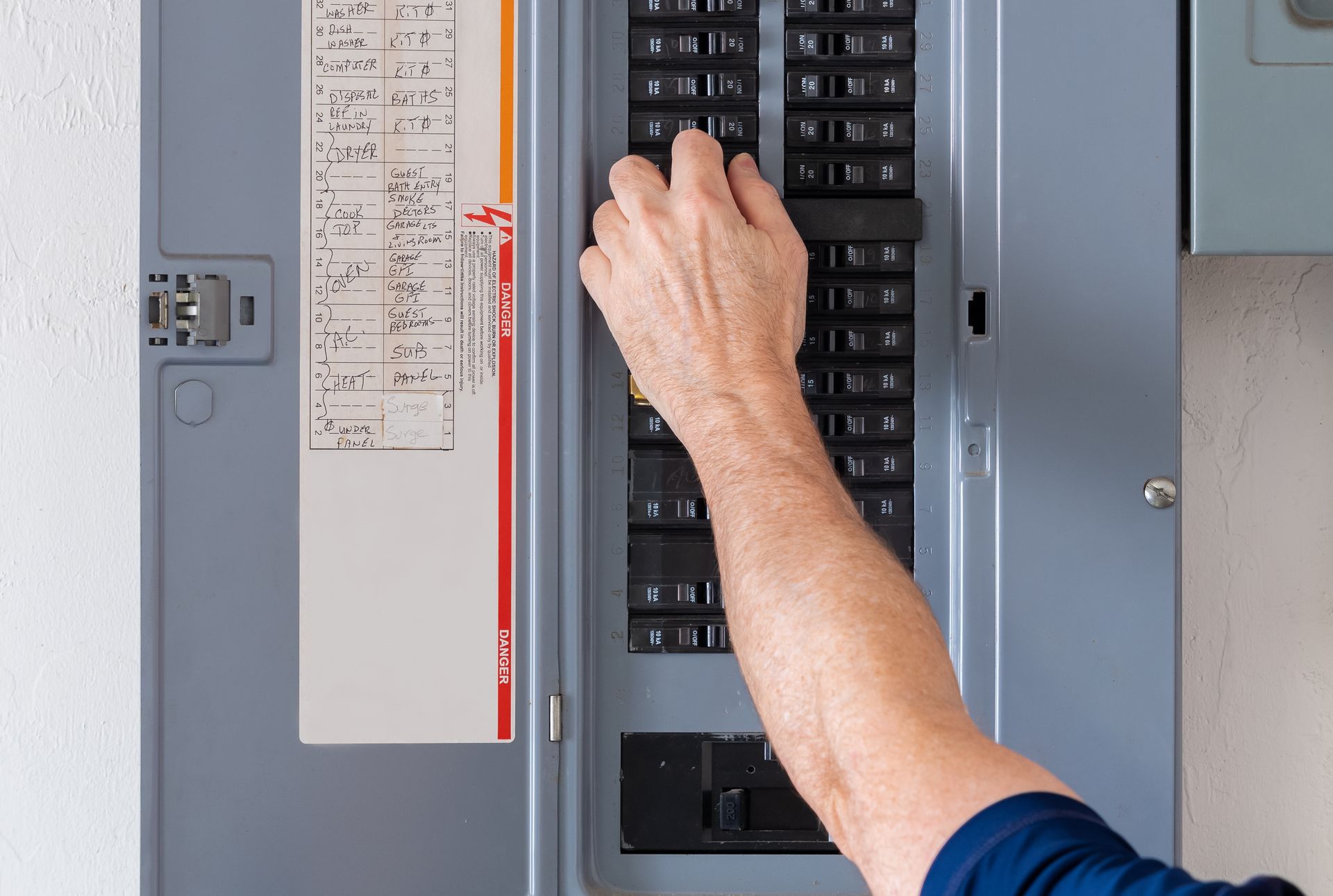 Hand reaching to reset tripped breaker in a residential electricity power panel.