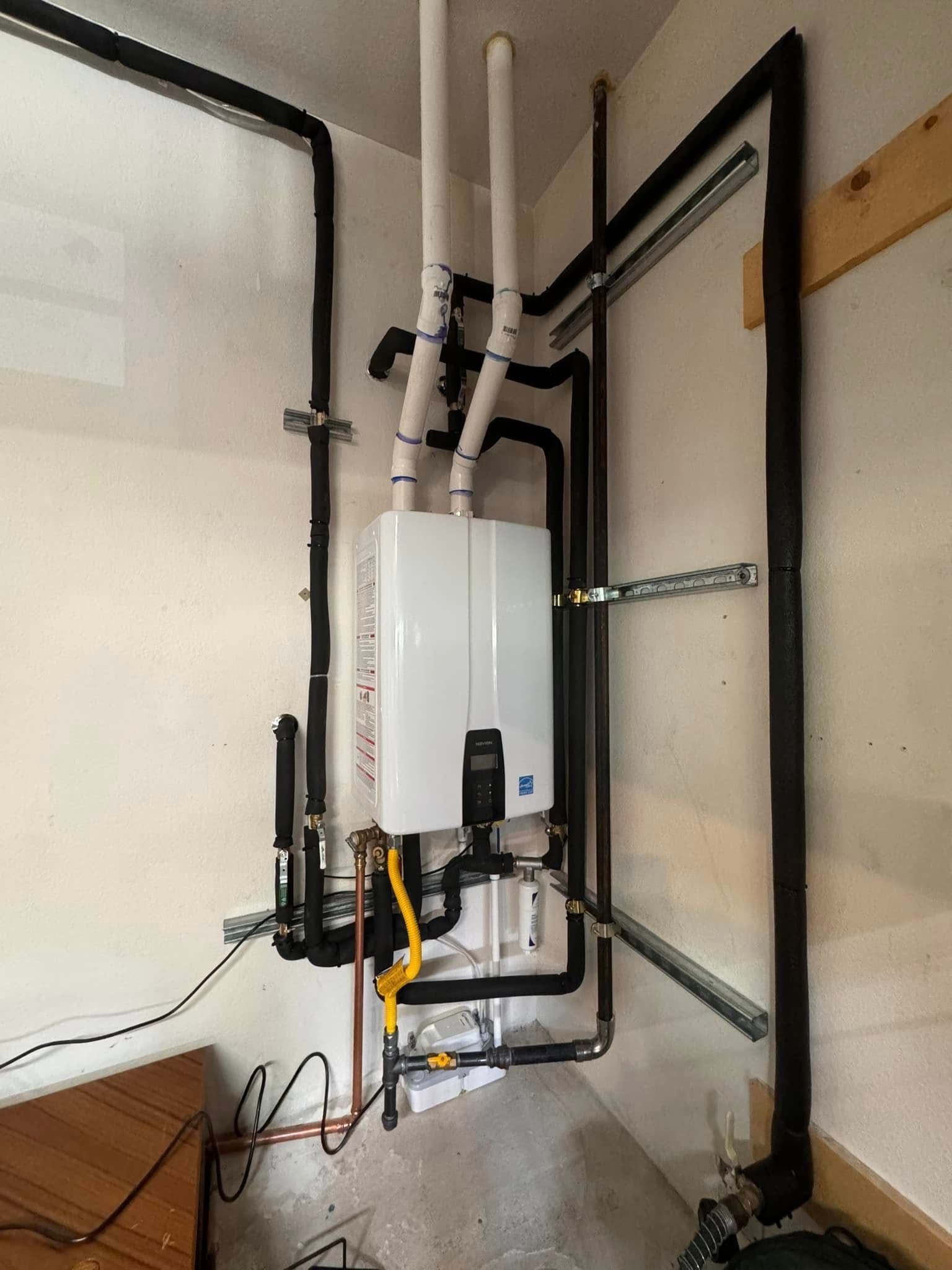 Tankless water heater installed on a wall with various pipes. Black insulation covers most pipes.