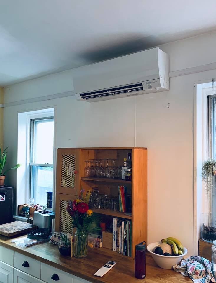 Kitchen with air conditioning unit above a wooden cabinet. Windows, countertop with fruit.