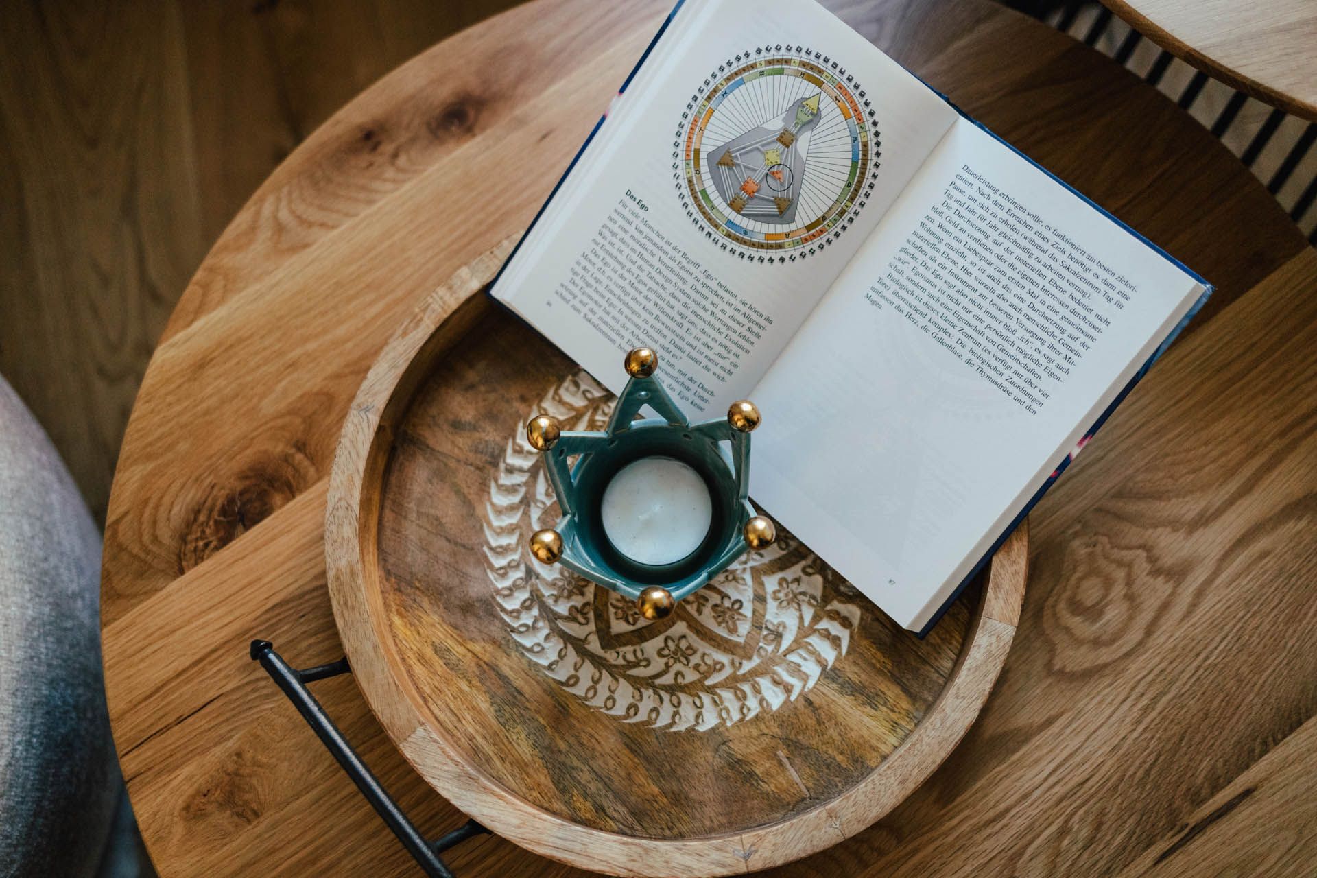 Auf einem Holztablett auf einem hölzernen Beistelltisch befinden sich ein offenes Buch, ein Kerzenhalter und ein Stift.