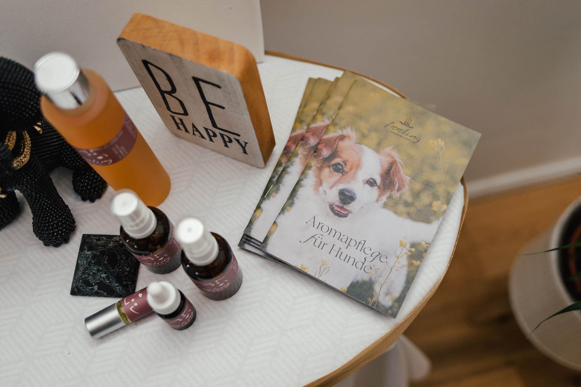 Tisch mit Aromaprodukten für Hunde, Holzblock mit der Aufschrift „BE HAPPY“ und ein Buch mit einem Hund auf dem Einband.
