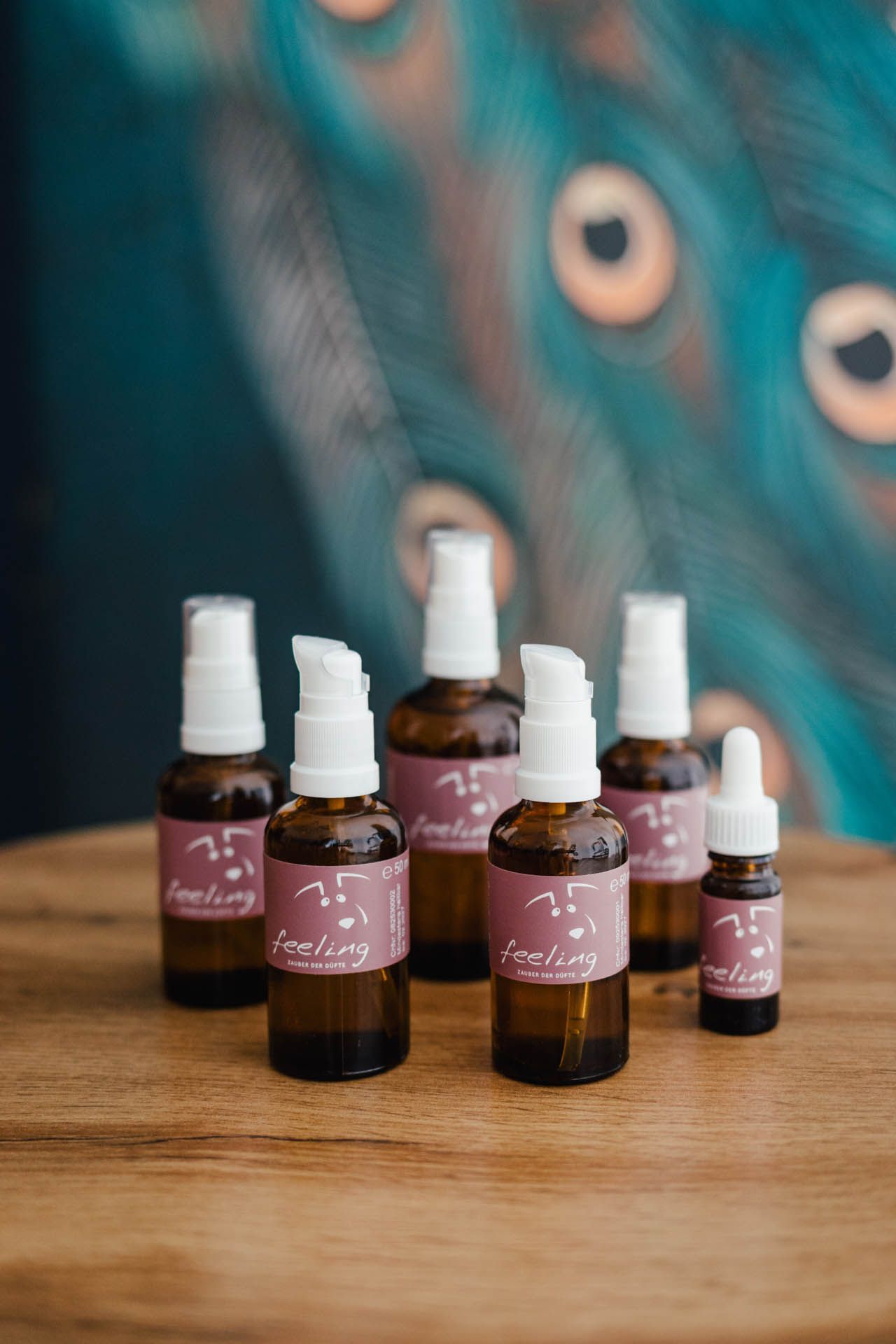 Glasflaschen mit weißen Pumpen und Etiketten, arrangiert auf einer Holzoberfläche vor einem Hintergrund aus Pfauenfedern.
