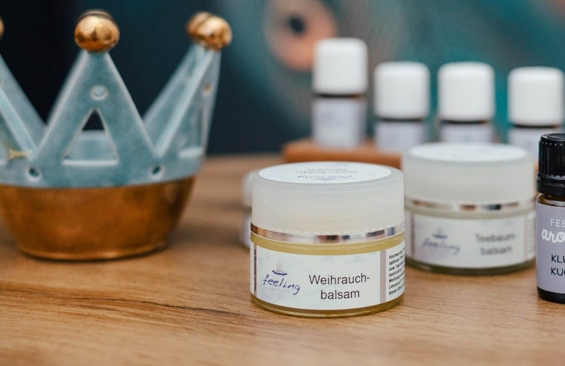 Glasbehälter mit Hautpflegeprodukten auf einer Holzoberfläche, im Hintergrund ein türkisfarbenes Kronenornament.