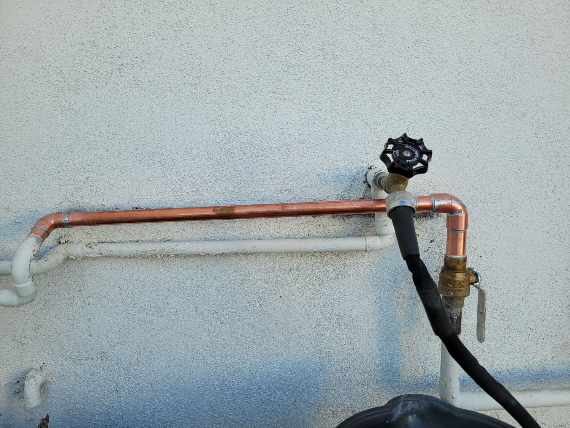 A hose is attached to a copper pipe on a wall