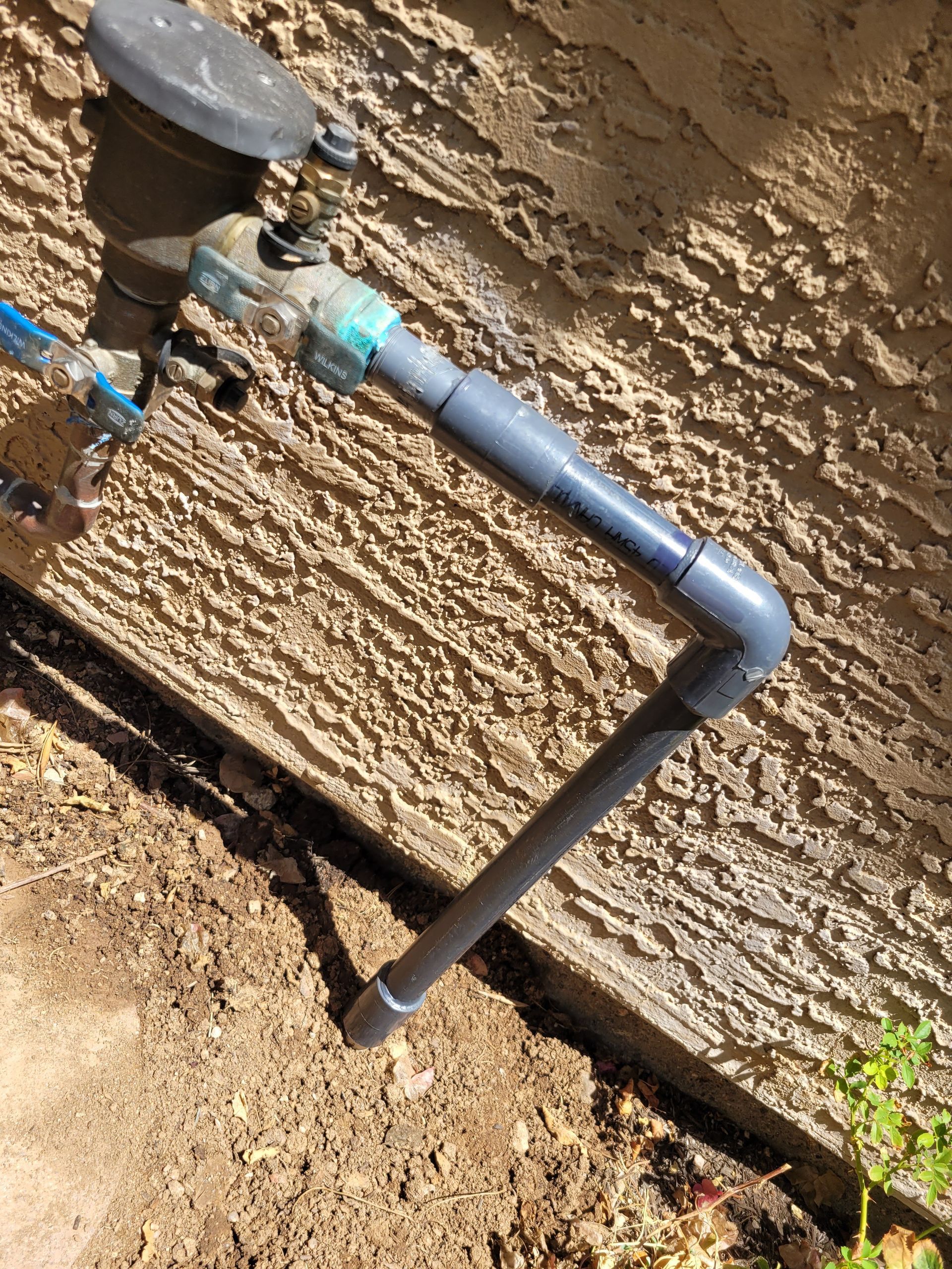 A water pipe is connected to a water meter on the side of a building.