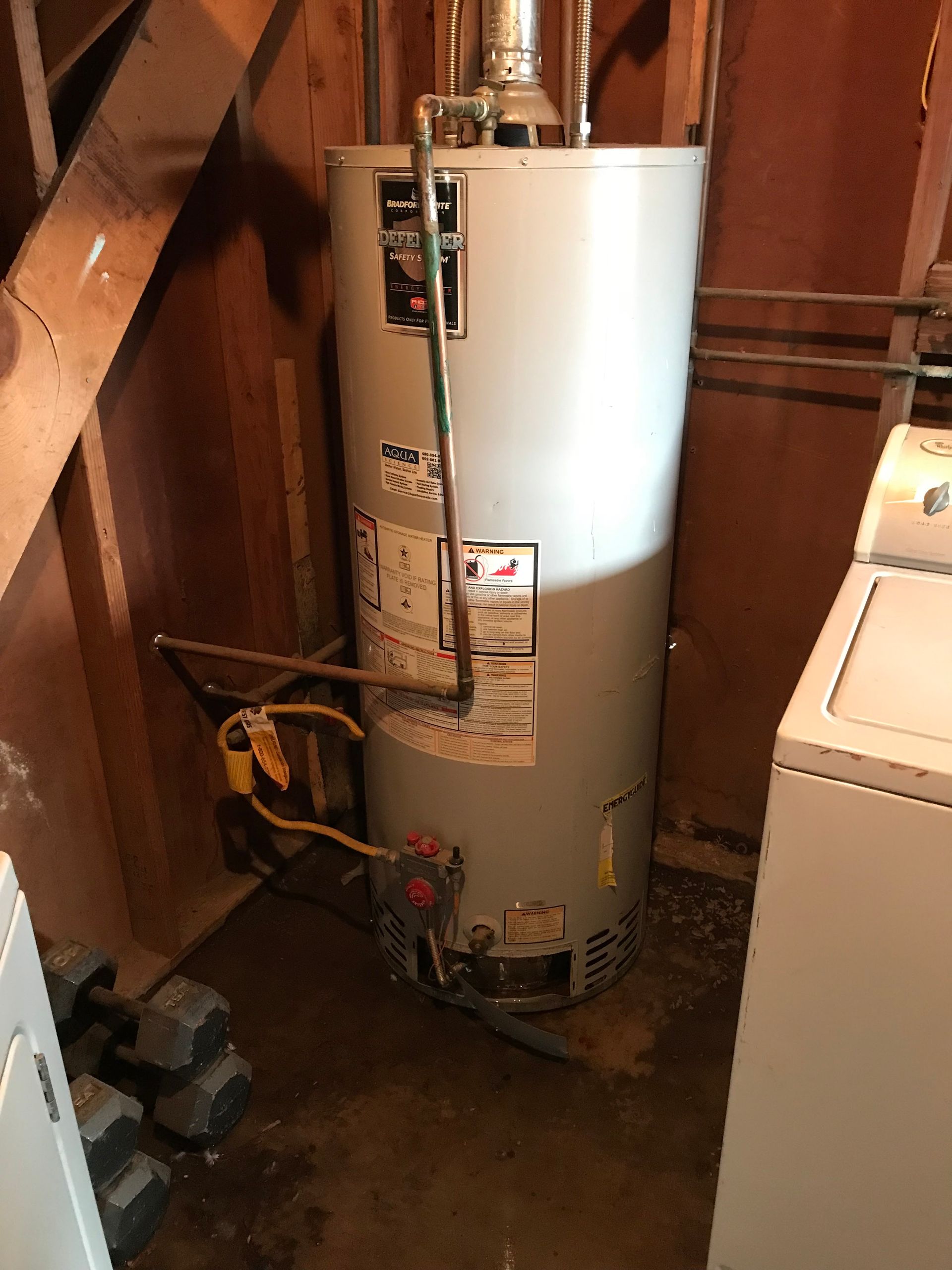 A water heater is sitting in a room next to a washer and dryer.