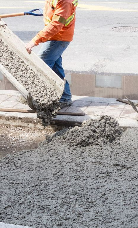 A Man is Pouring Concrete on a Sidewalk With a Shovel — Copp & Co Civil & Plant Hire in Cannonvale, QLD