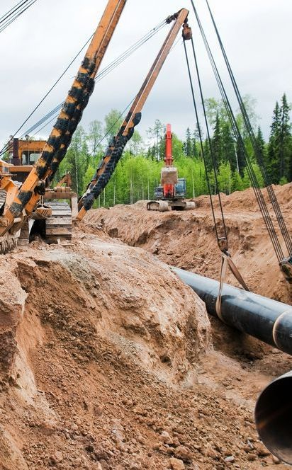 A Crane is Lifting a Large Pipe in the Dirt — Copp & Co Civil & Plant Hire in Airlie Beach, QLD