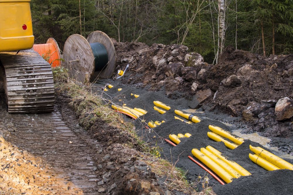 A Yellow Excavator is Digging in the Dirt Near a Pile of Yellow Pipes — Copp & Co Civil & Plant Hire in Cannonvale, QLD