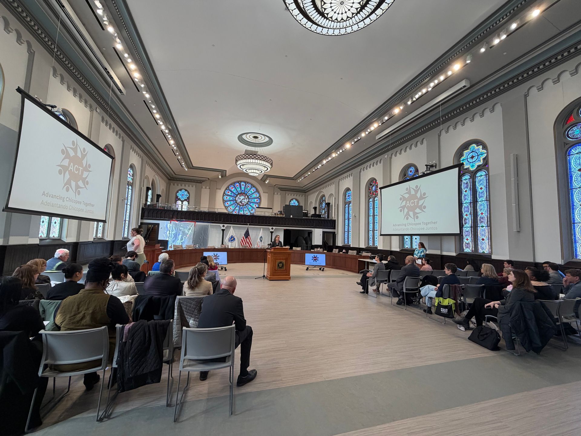 ACT press event, people seated listening to person at podium, ACT logo on large screen