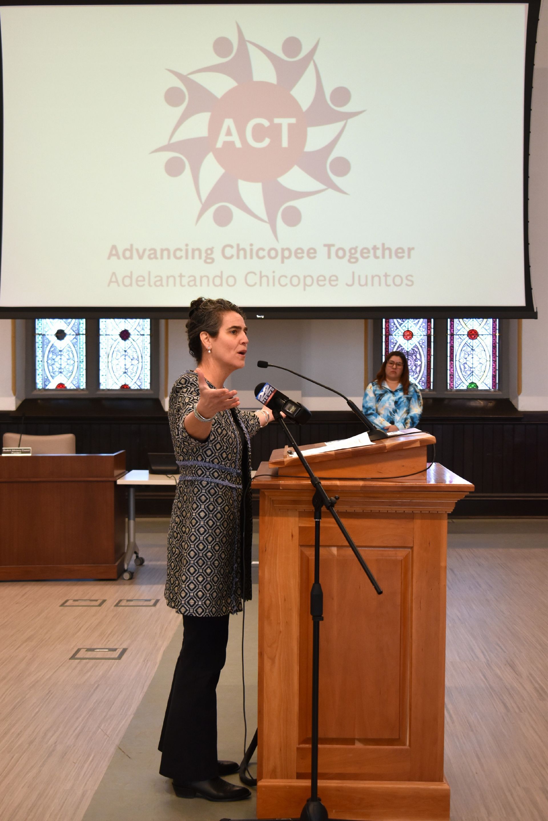 Jessica Collins speaking at podium with ACT logo on screen next to her