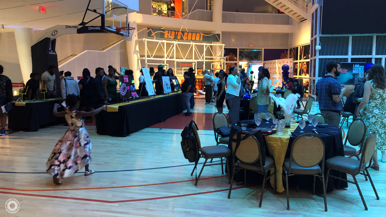 Youth stand next to data visualizations, attendees mingling, fancy table with gold table cloth and feather decorations