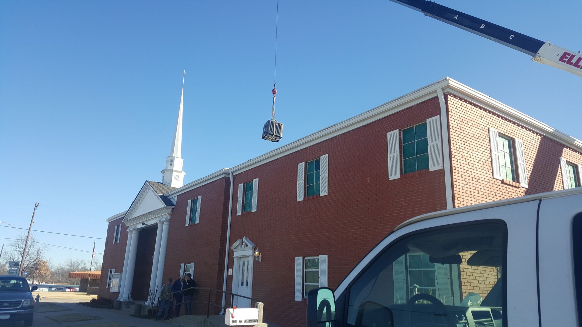 A white van is parked in front of a large red brick building.