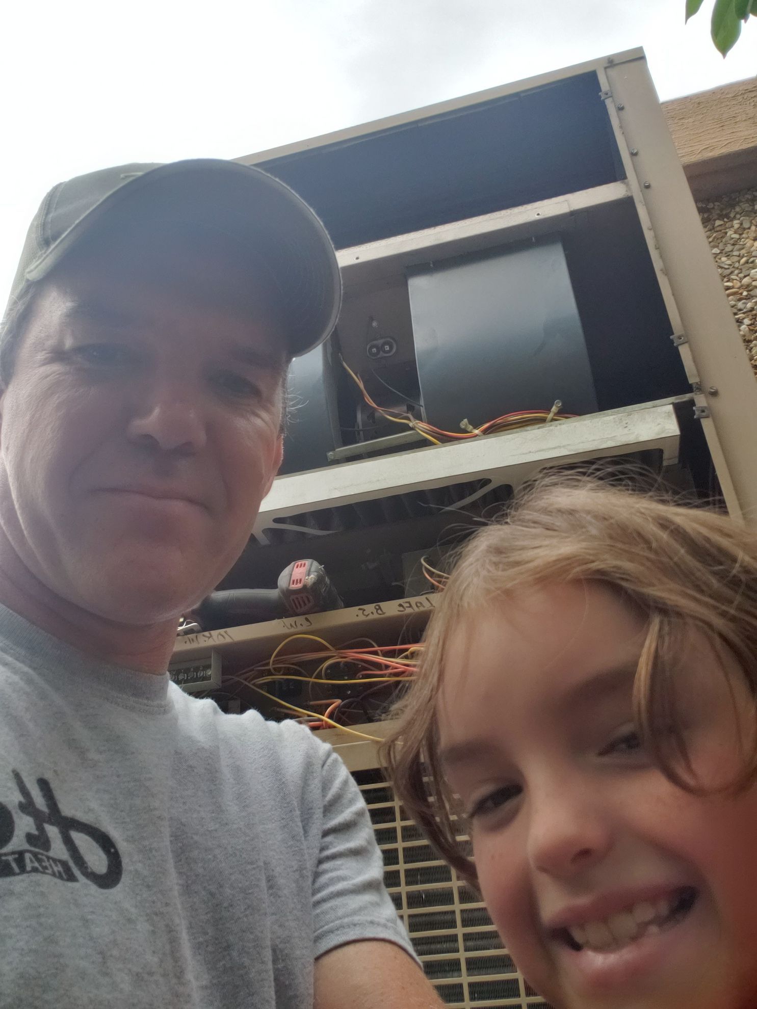 A man and a little girl are posing for a picture in front of an air conditioner.
