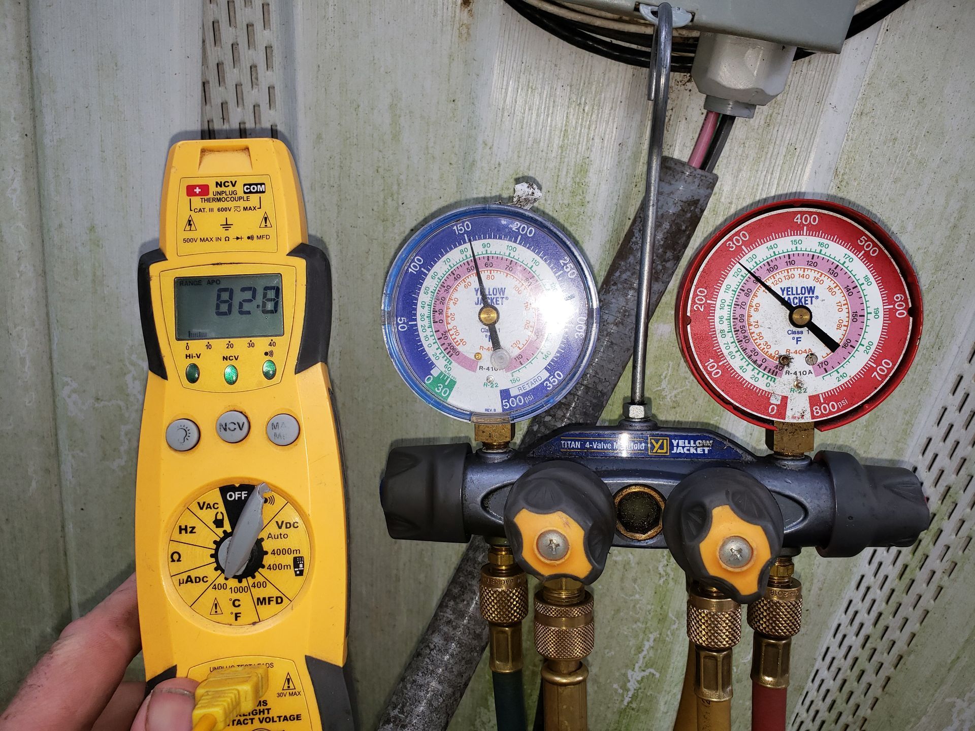 A man is holding a digital multimeter next to a couple of gauges