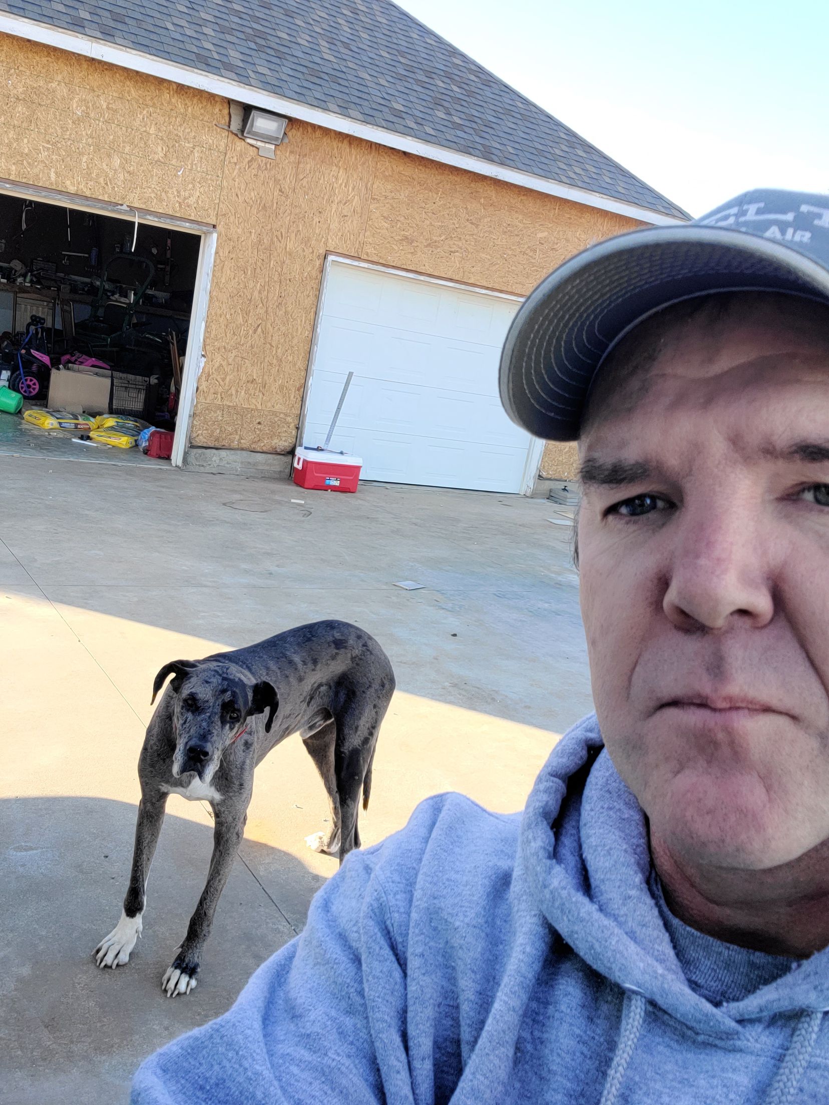 A man is taking a selfie with his dog in front of a garage.