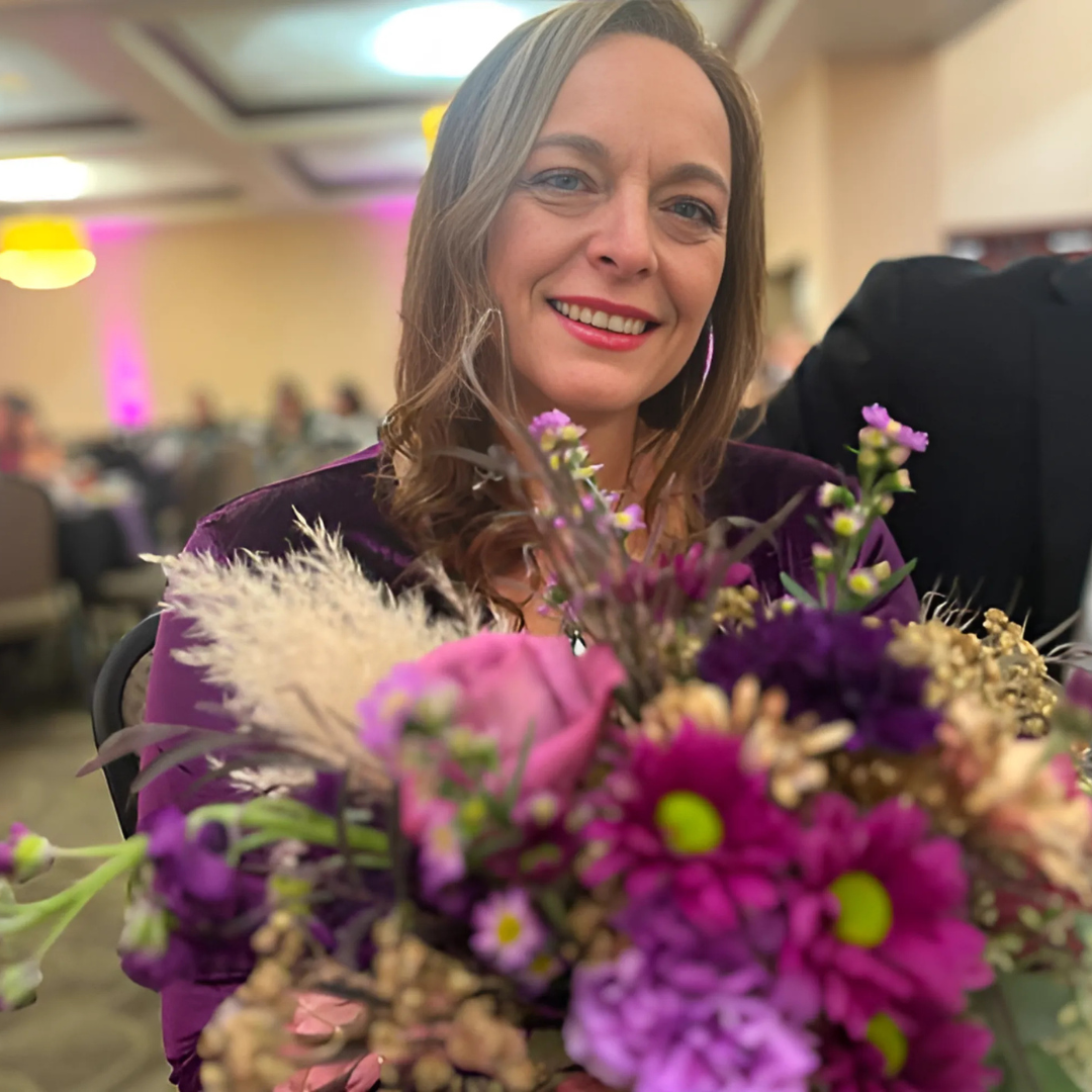 A woman is holding a bouquet of purple flowers and smiling