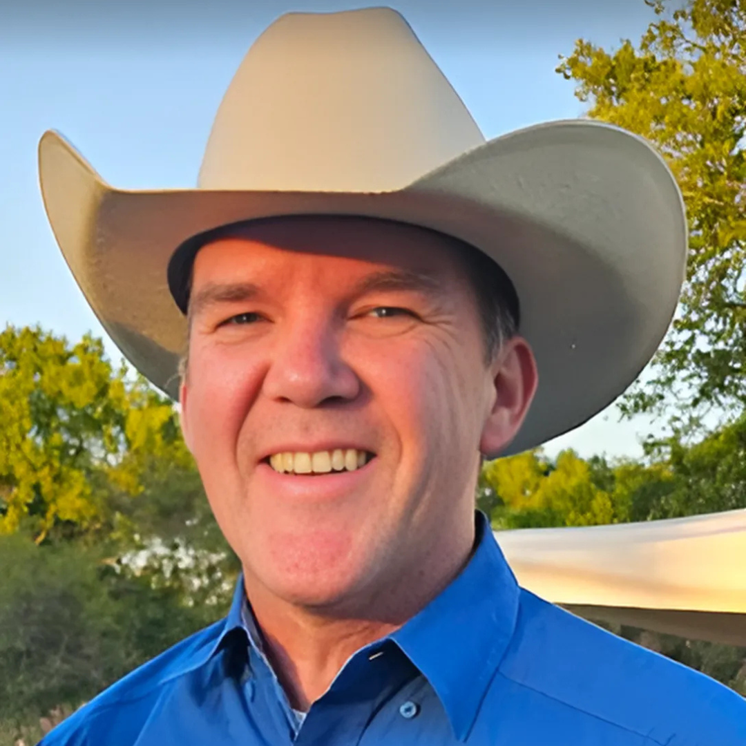 A man wearing a cowboy hat and a blue shirt is smiling