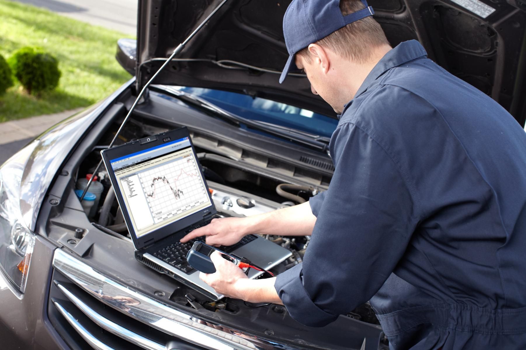 Mechanic in blue uniform, using laptop to diagnose a car engine.