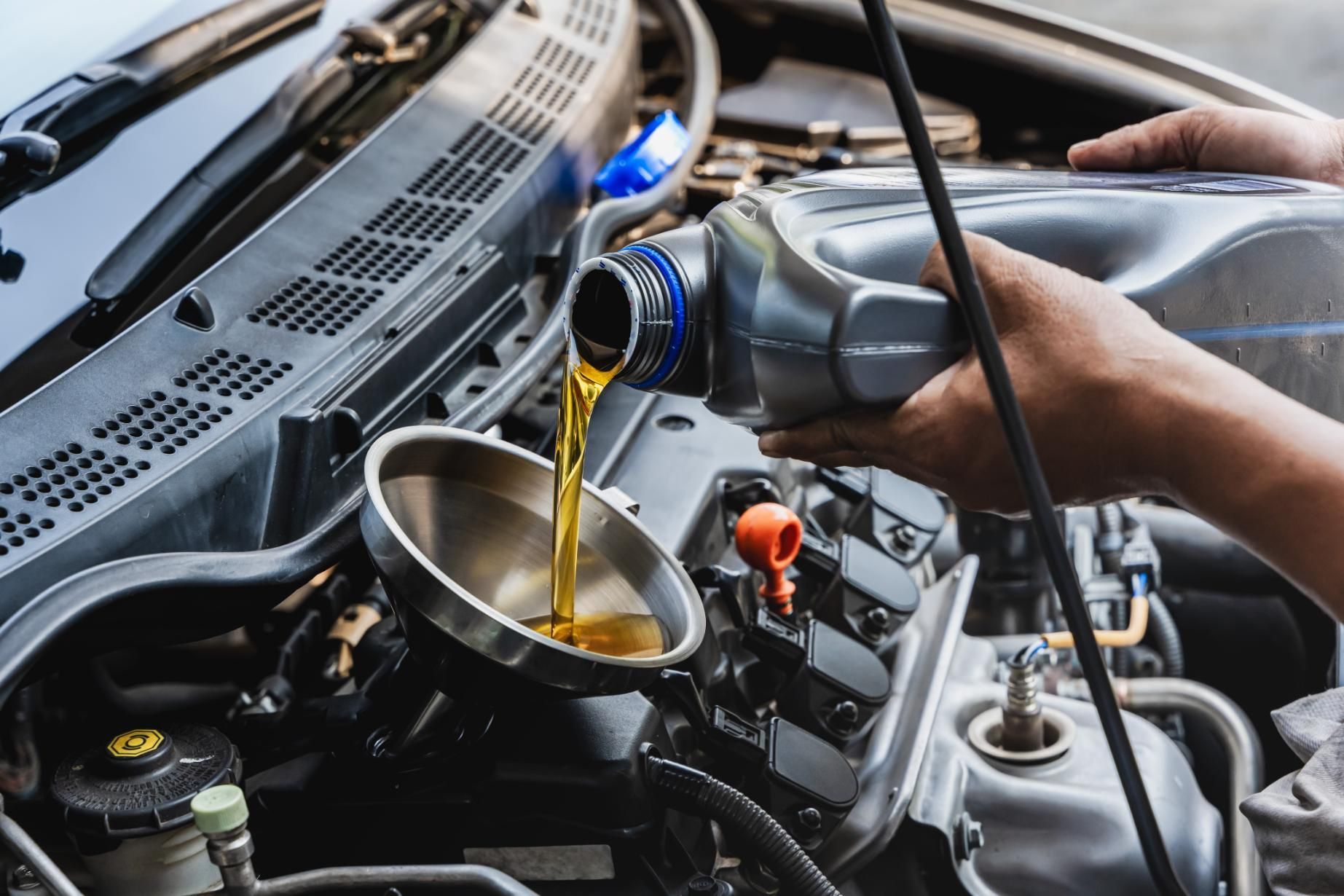 Hands pouring oil into a car engine, using a funnel, in a well-lit mechanic setting.