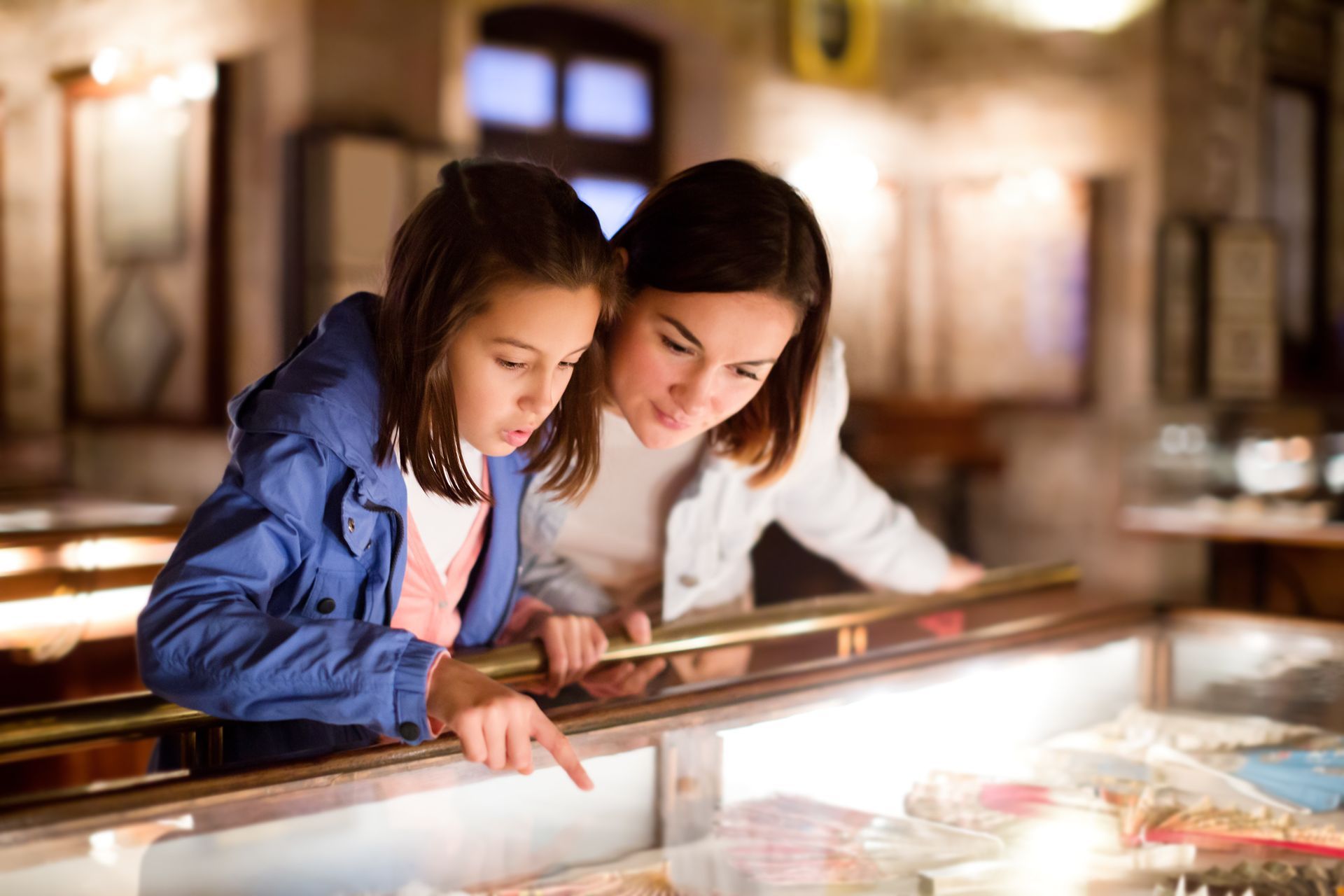 A woman and a little girl are looking at a display case in a museum.
