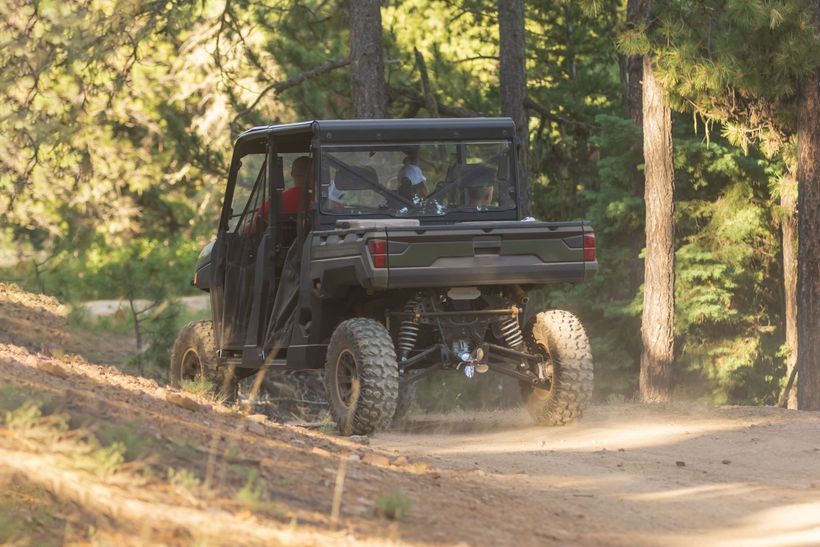 A atv is driving down a dirt road in the woods.