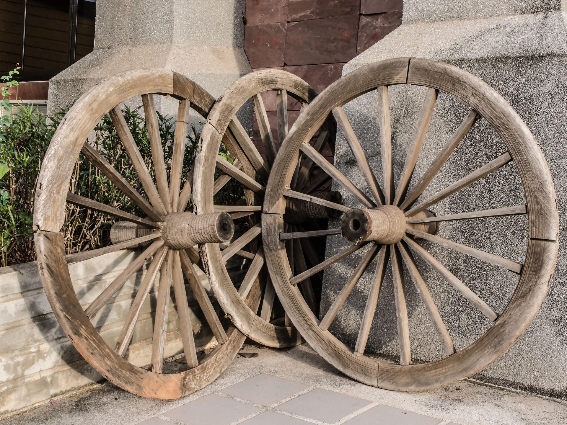 Two wooden wagon wheels are sitting next to each other on a sidewalk.