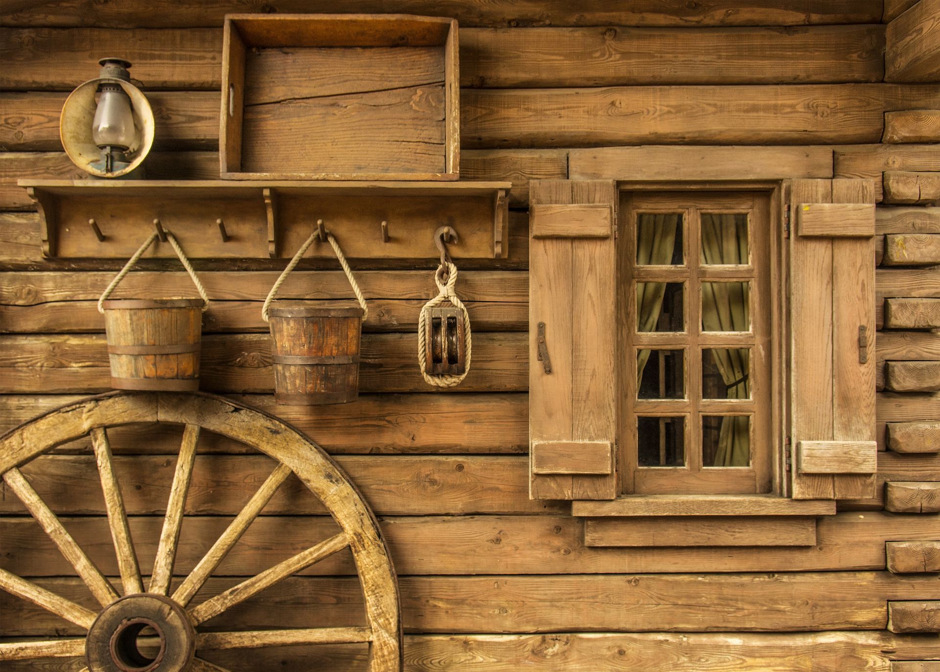 A wooden cabin with a wagon wheel and buckets on the wall.