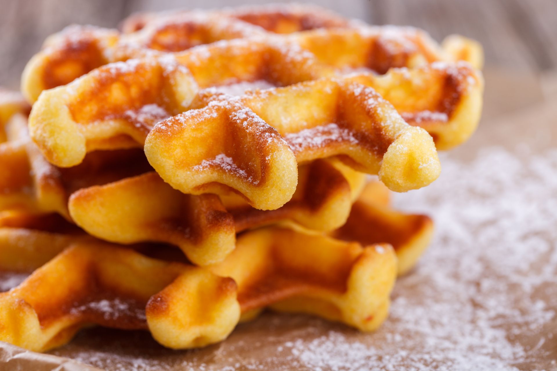 A close up of a stack of waffles with powdered sugar on a wooden table.