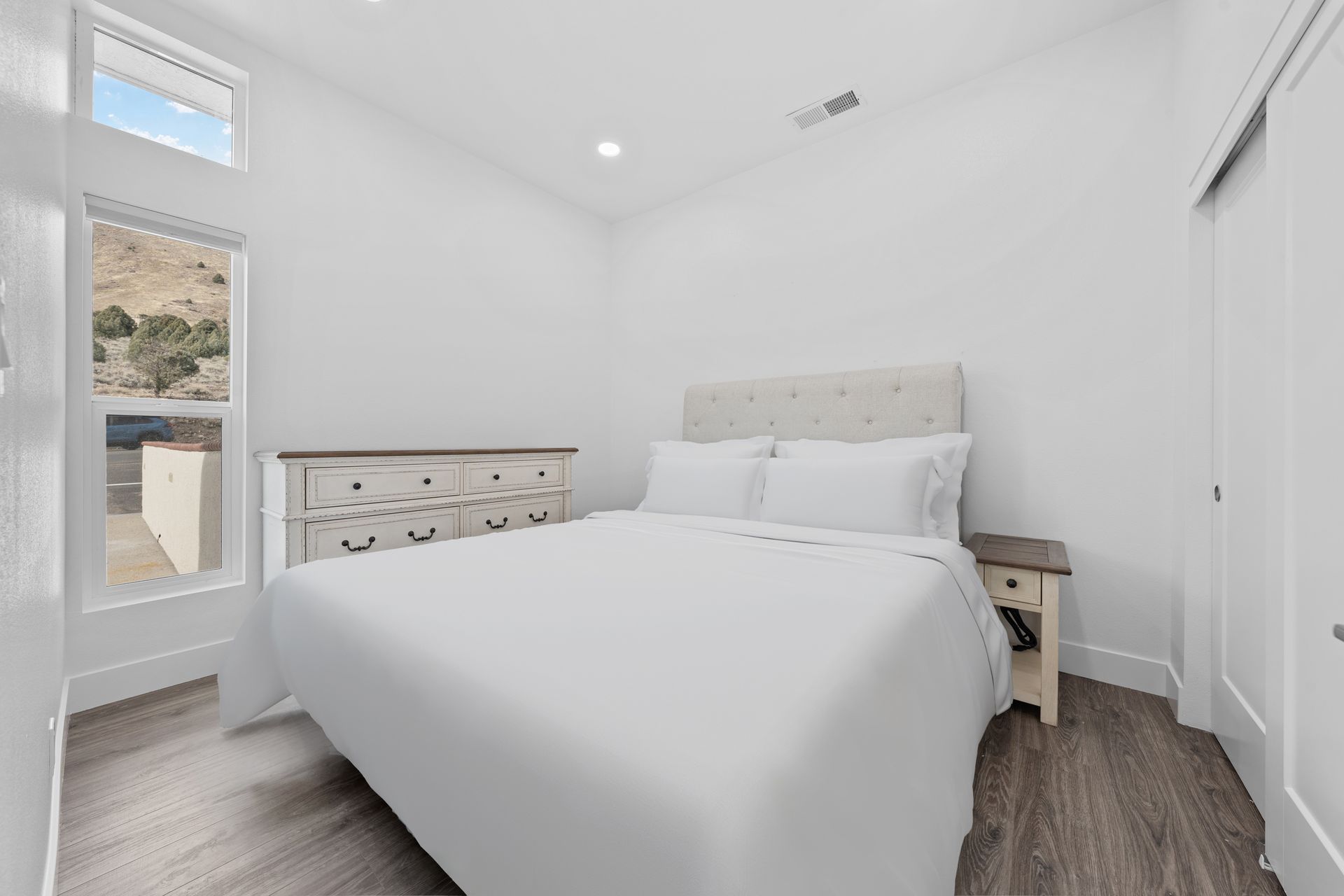 A bedroom with a bed , dresser , nightstand and window.