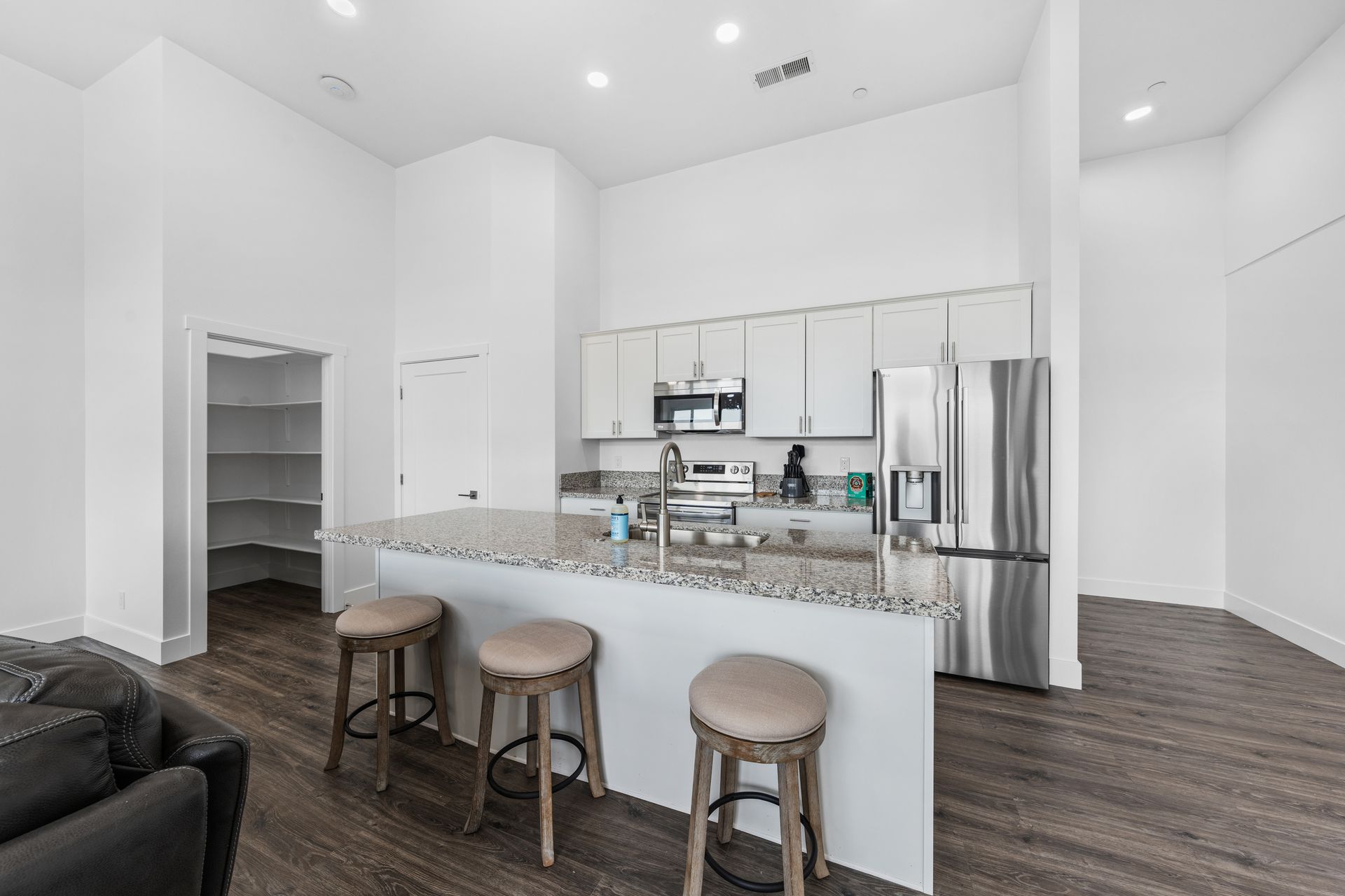 A kitchen with white cabinets and stools and a stainless steel refrigerator.