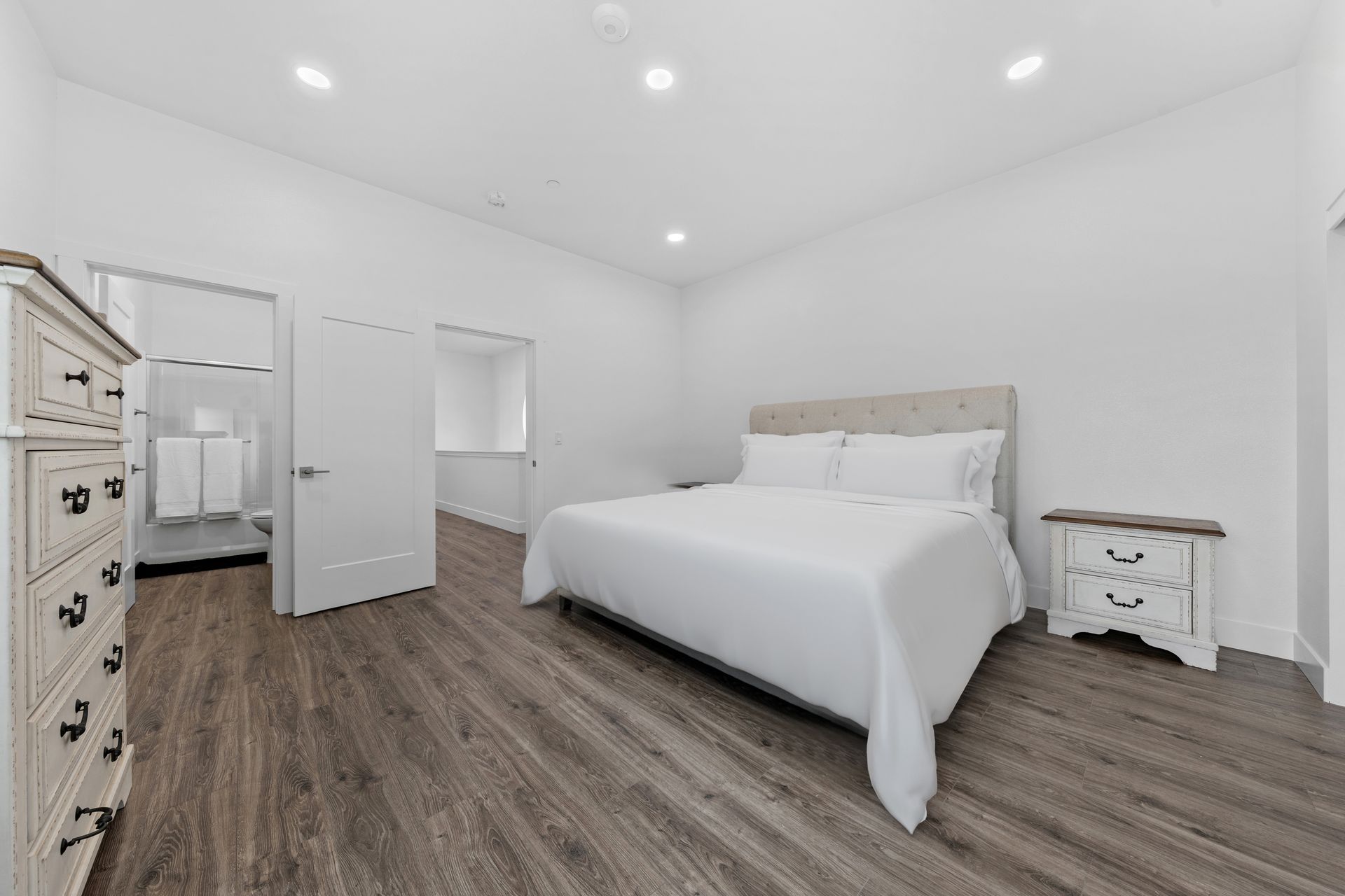 A bedroom with a king size bed , dresser , nightstand , and hardwood floors.