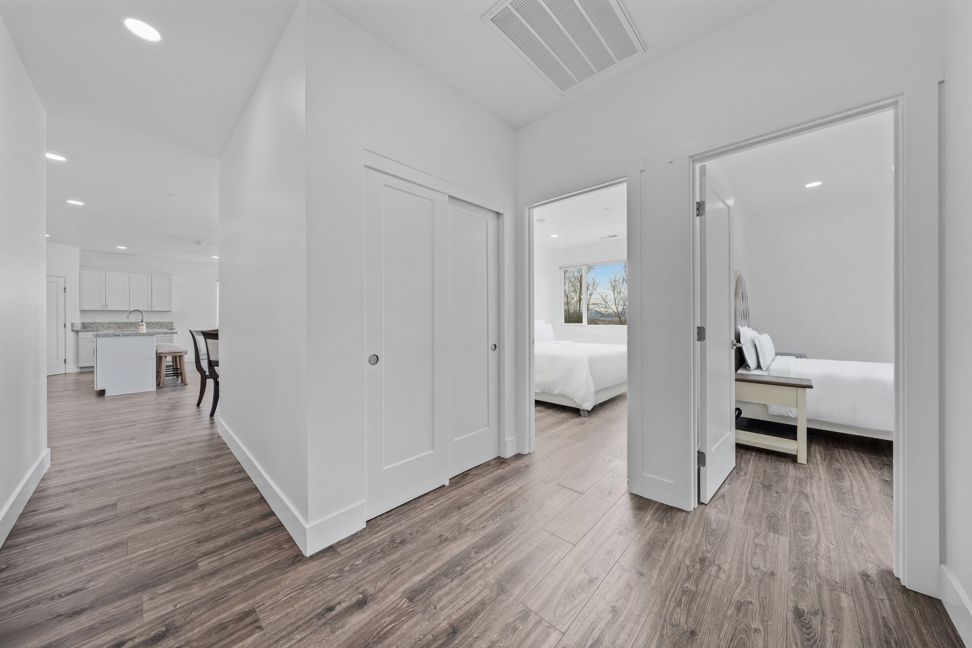A hallway leading to two bedrooms in a house with hardwood floors.
