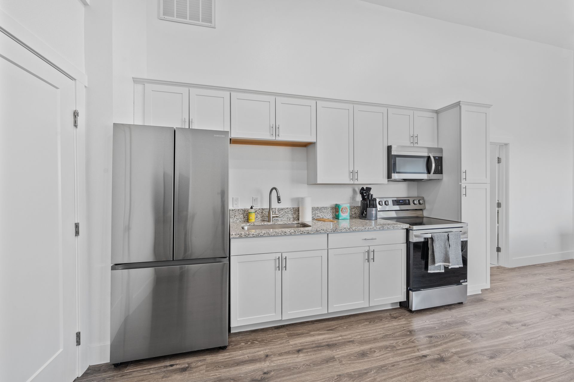 A kitchen with white cabinets , stainless steel appliances , a refrigerator , stove , microwave and sink.