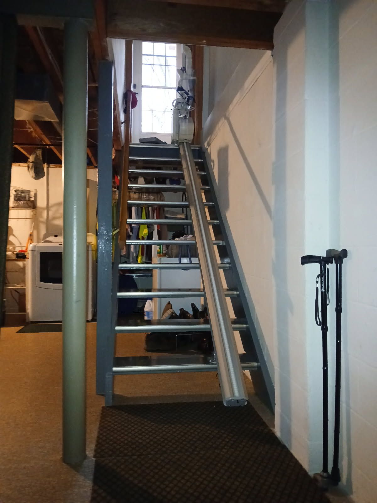 Staircase with a stair lift in a basement.  Two canes are leaning against the white wall to the right.