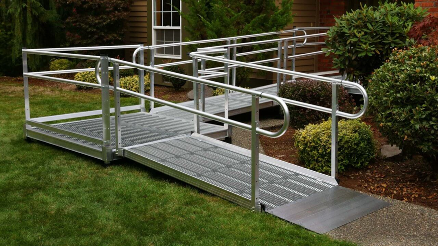 Aluminum wheelchair ramp with handrails in a yard leading to a house.