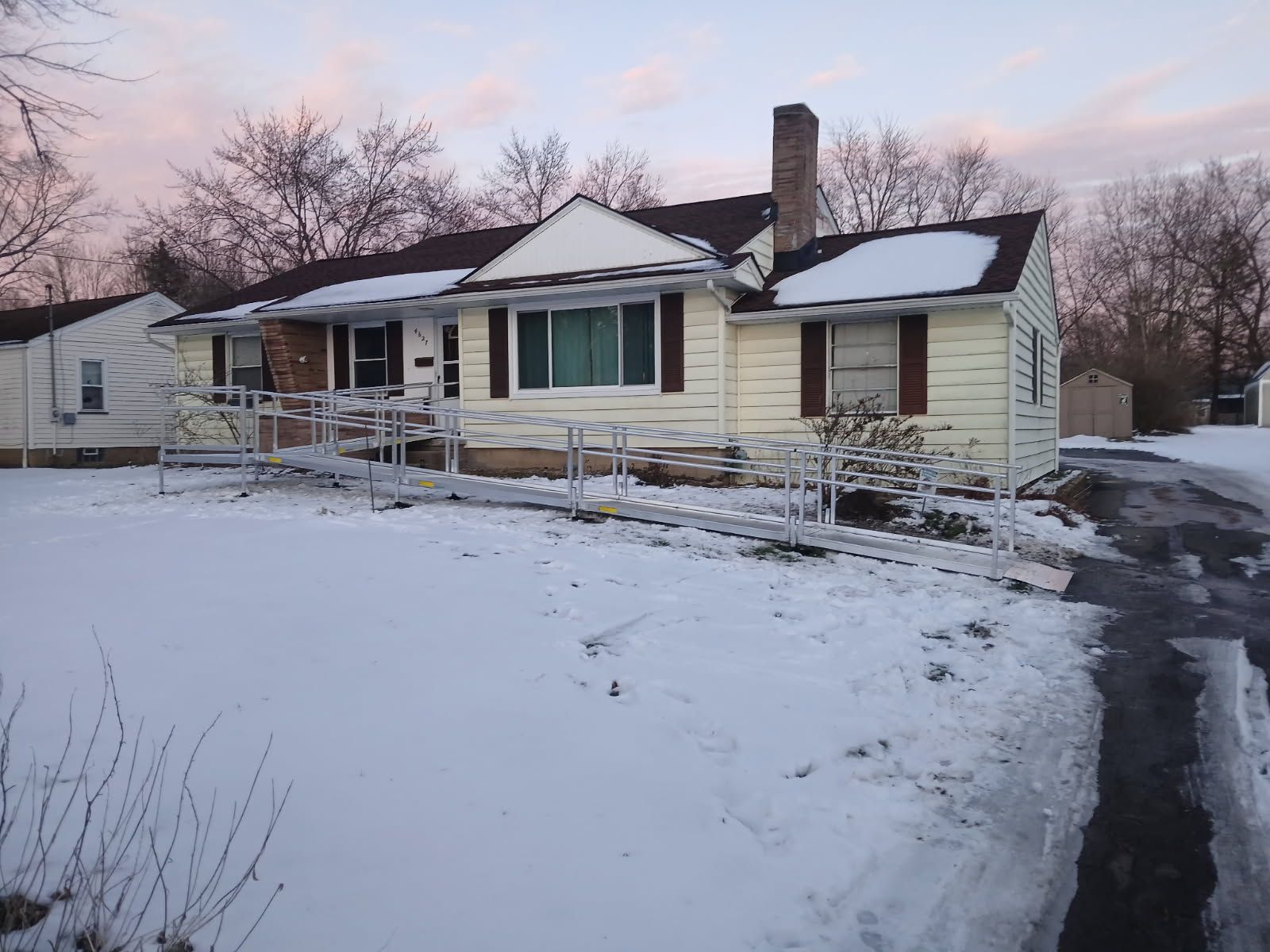 A one-story house covered in snow with a ramp. Winter scene with a cloudy sky.