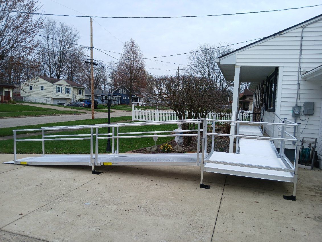 Aluminum ramp for wheelchair access to a white house's front porch, on a gray overcast day.