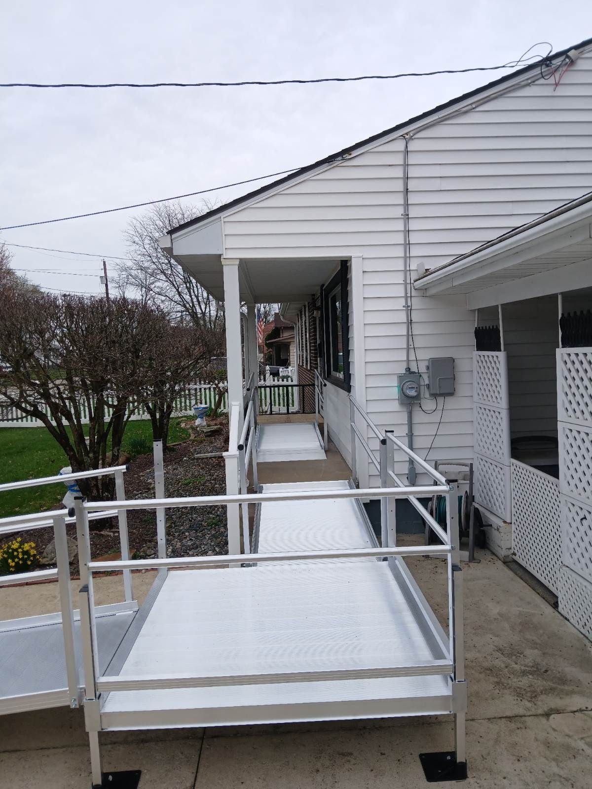 Aluminum ramp leading to a white building with a porch and accessible features. Cloudy sky overhead.