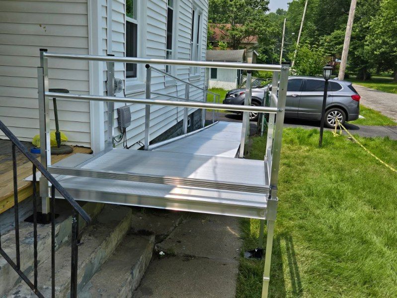 Wheelchair lift and ramp attached to the front porch of a house. Silver metal construction.