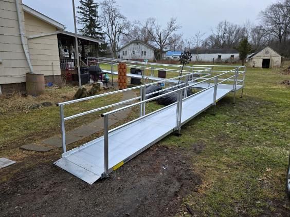 Aluminum wheelchair ramp leading up to a beige house in a grassy yard.