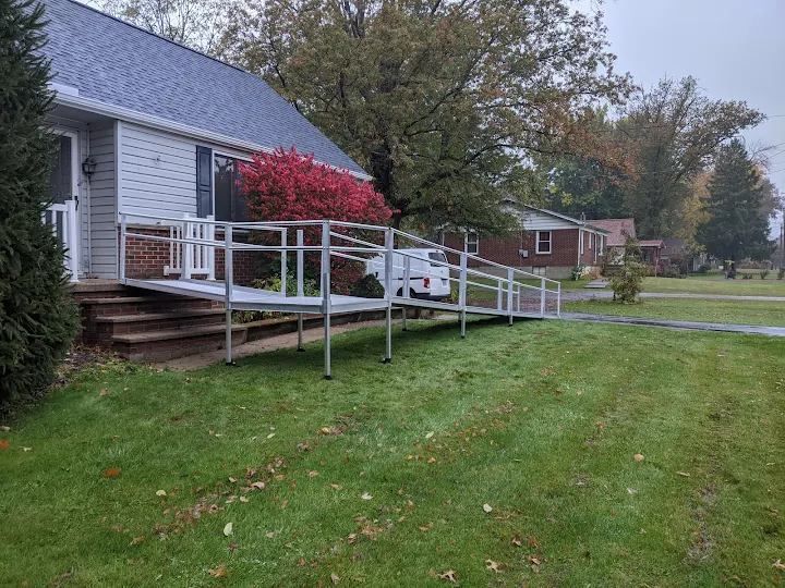 A residential building with a wheelchair ramp over grass.  The ramp is silver, leading to a front porch.